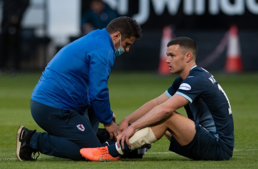 Ross Matthews sits on the ground as he is given treatment by the Raith Rovers physio in 2021.