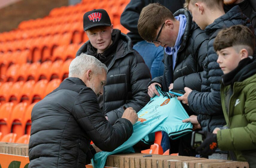 Dundee United manager Jim Goodwin signs away shirt for fan.
