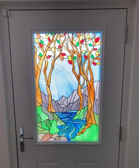 Beautiful stained glass window in a door depicting a forest scene with trees, hills and a river