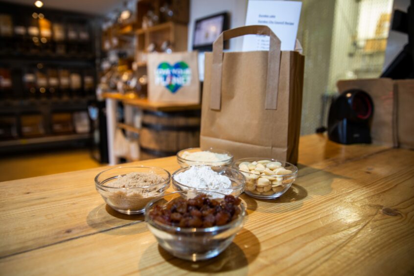 Ingredients laid out on the wooden counter in a zero waste shop. Raisins, ground almonds, flour and whole almonds in small, glass bowls. All needed for baking a Dundee Cake for the King's Coronation.