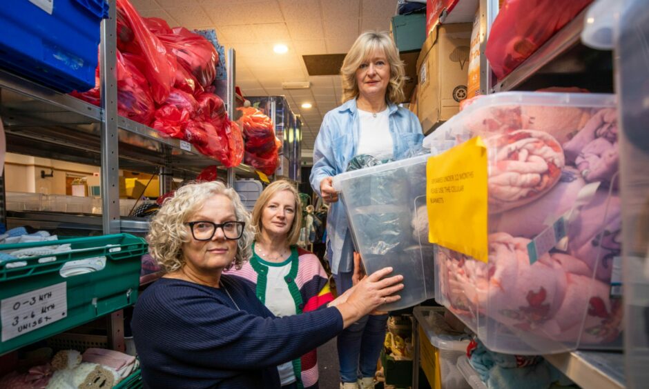 Togs for Tots volunteer Angela Giacchetto, secretary Pauline MacDougall and chair Jill Smith moving boxes in storage room.