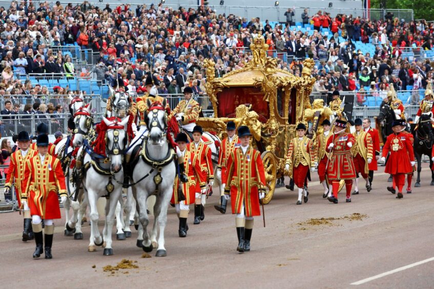 Gold state coach pulled by white horses and flanked by royal attendants in ceremonial gear