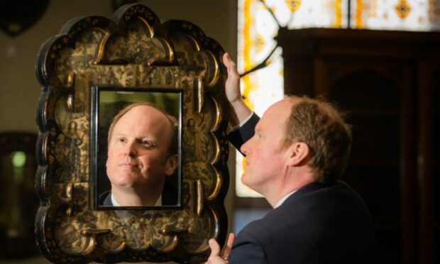 Auctioneer Nick Burns with the 16th-century stumpwork and lacquer mirror dated 1652 featuring Charles II.