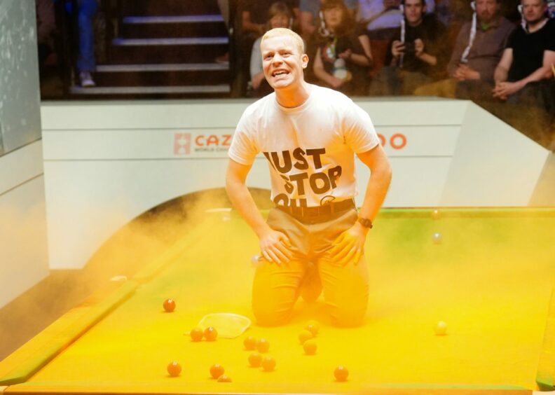 Man in Just Stop Oil t shirt in a haze of orange powder on top of a snooker table