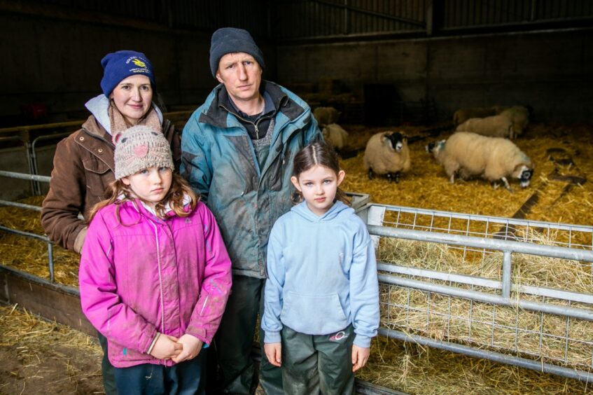 Farmer Stuart McDougall with his wife and two young daughters in a shed with some sheep