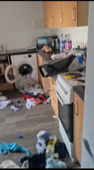 Trashed kitchen strewn with clothing and other belongings.