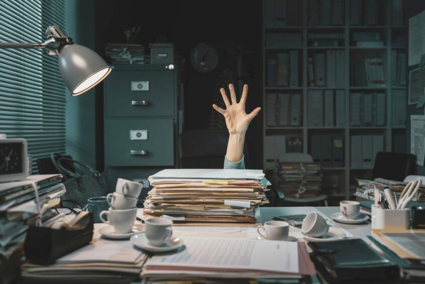 Office worker and desk surrounded by empty coffee cups and a pile of paperwork.