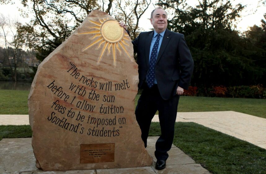 Alex Salmond next to s large rock on which the words 'the rocks will melt with the sun before I allow tuition fees to be imposed on Scotland's students' are carved.