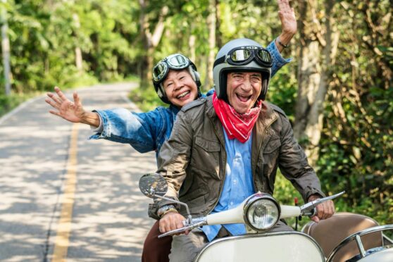 Senior couple happily riding a classic scooter, showing they're ready for retirement