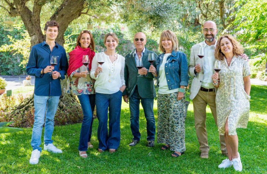 A family of seven holding wine glasses while standing in a garden.