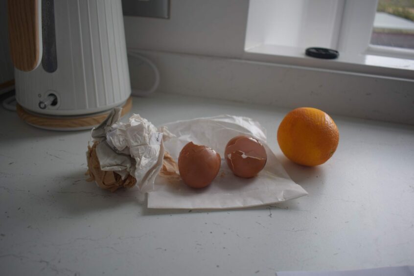 Brown and white paper scrunched in a ball, two egg shells and an orange. 