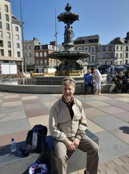 Jim Spence sitting in the sunshine next to a fountain.