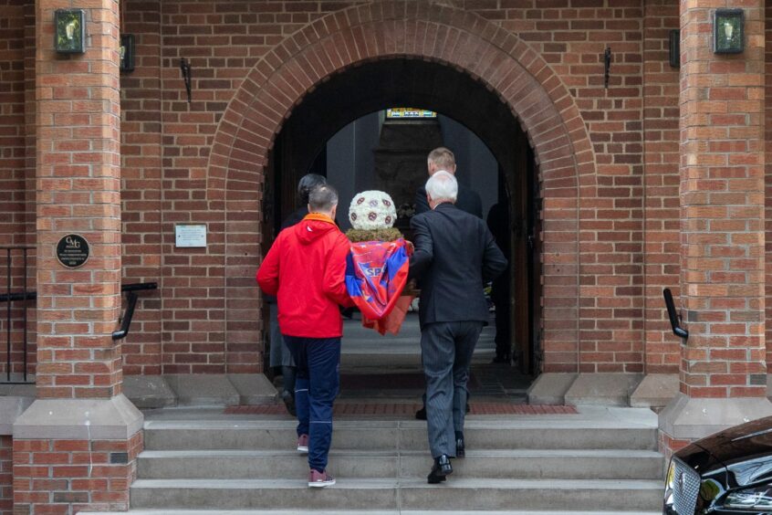 Jack Stewart's coffin being carried into Dundee Crematorium covered in the red and blue colours of Dundee West
