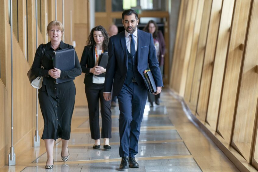 First Minister of Scotland Humza Yousaf and Deputy First Minister Shona Robison walk through a corridor at the Scottish Parliament.