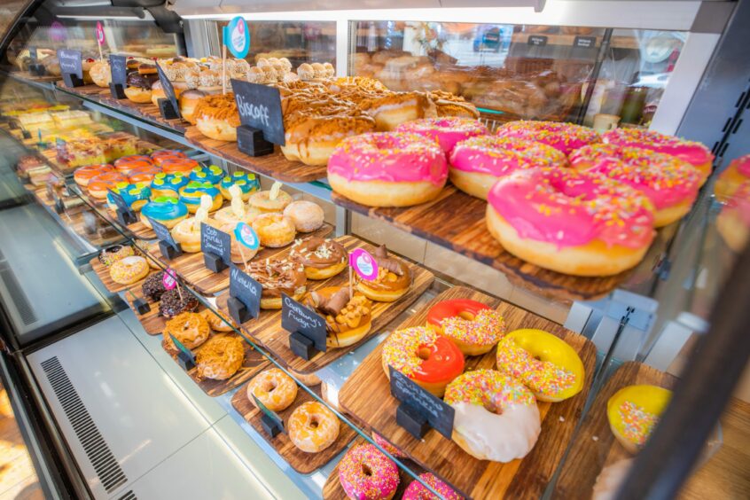 Inside a bakery counter with three shelves of colourful doughnuts.