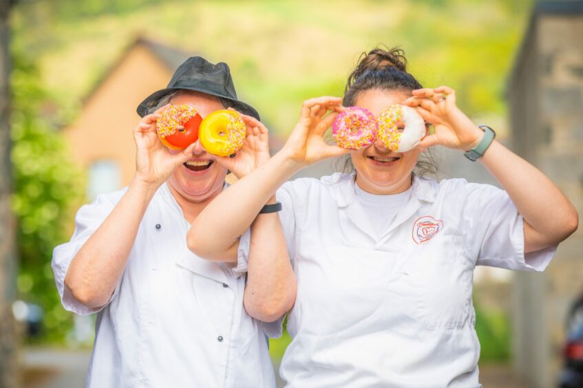 Two female bakers holding colourful doughnuts in front of their eyes.