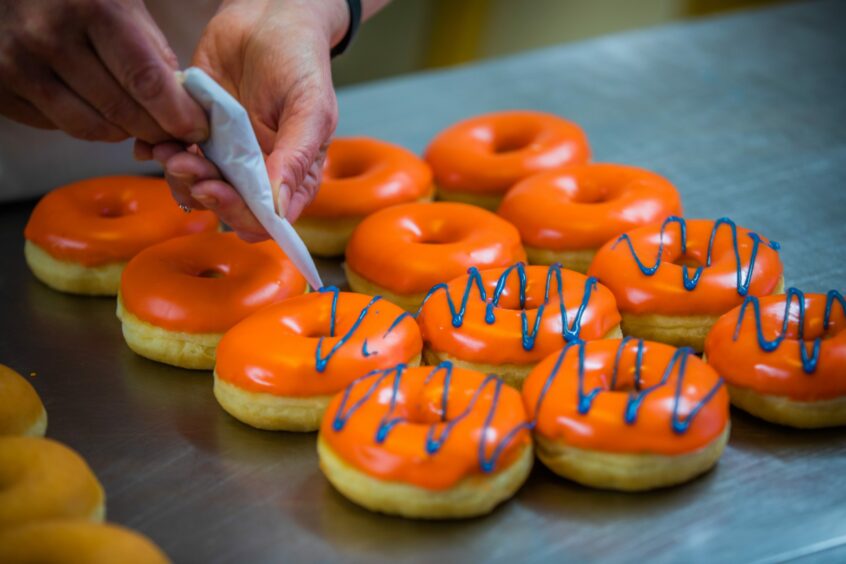 A tray of orange glazed doughnuts with blue decorations.