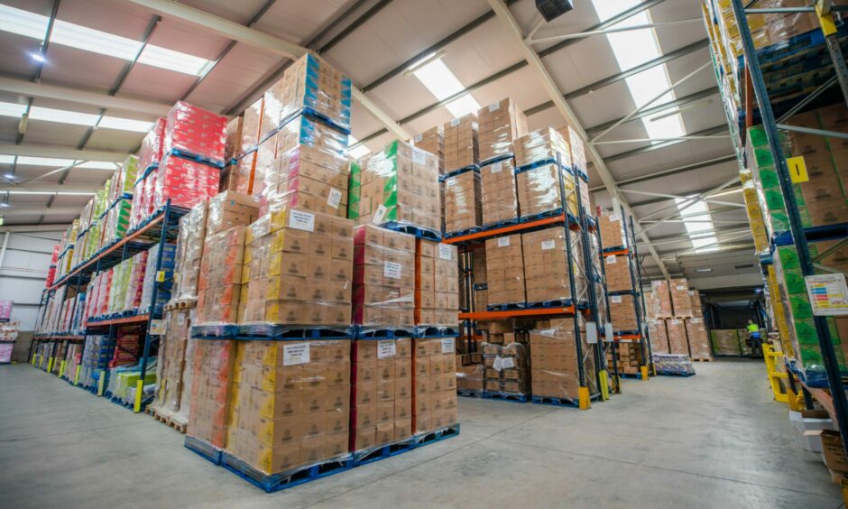 A warehouse with boxes containing bags of crisps are stacked high.