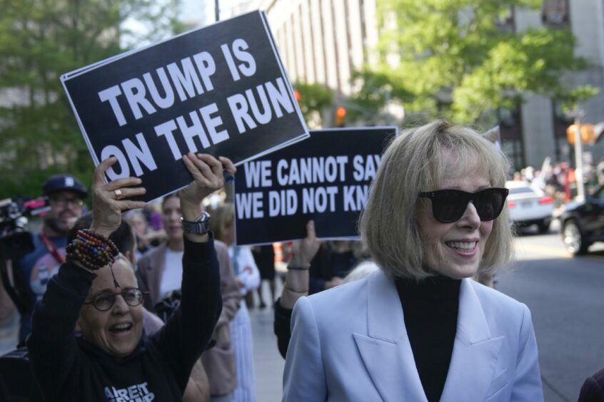 E Jean Carrol in a crowd of protesters waving signs with slogans such as 'Trump is on the run'.