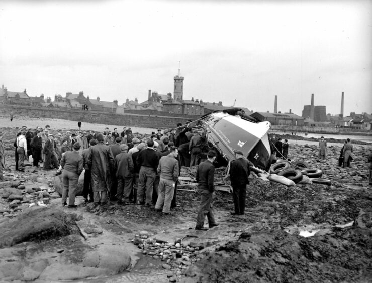 Black and white photo showing the Arbroath lifeboat the Robert Lindsay capsized on the foreshore surrounded by a large crowd of onlookers following the disaster in 1953.