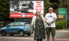 A man and woman standing in front of an electronic billboard, carrying an appeal over the death of a boy in a crash in 1989