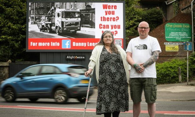 A man and woman standing in front of an electronic billboard, carrying an appeal over the death of a boy in a crash in 1989.