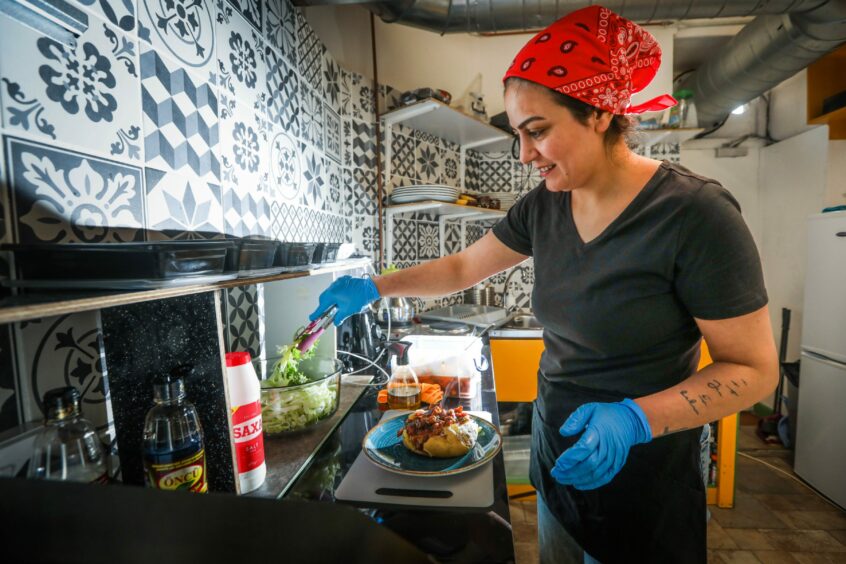 A woman wearing a red headscarf inside a vegetarian kitchen preparing a jacket potato.