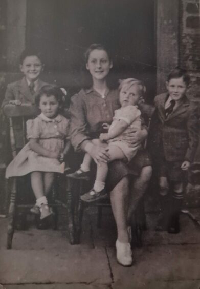 Black and white family photo from late 1940s, showing a little girl, seated to a young woman holding a toddler on her lap with two small boys standing behind them.
