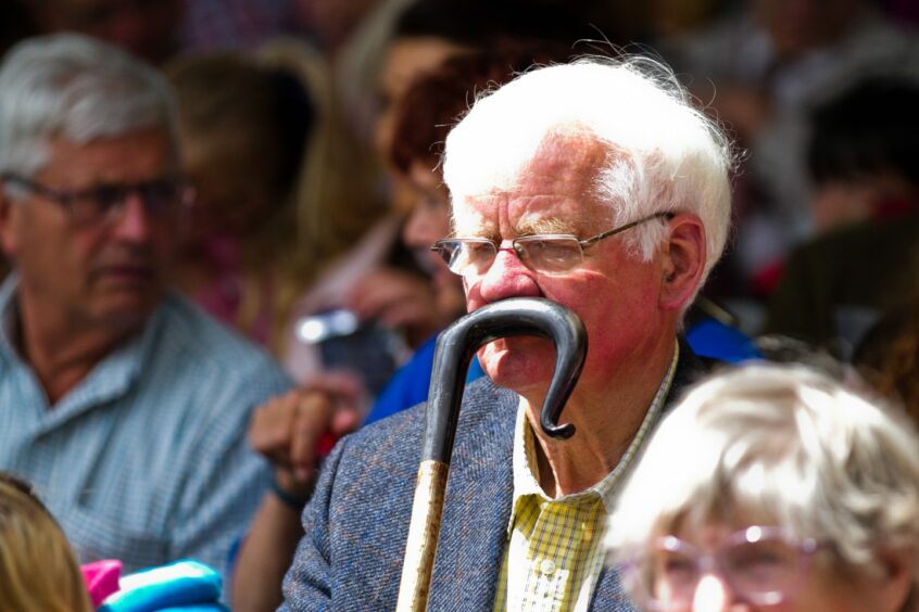 man with a shepherds crook in front of his face in the Highland Show crowd.