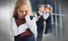 Schoolgirl looking frightened with bullies whispering behind her.