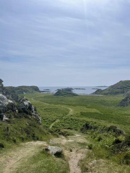 scenic view of path leading down through rocks and bracken to St Columba's Bay, Iona, and out to sea on a sunny day.