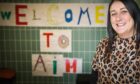 Anxiety in Motion (AIM)’s principal teacher Jenna Yule in front of a "Welcome to AIM" sign.