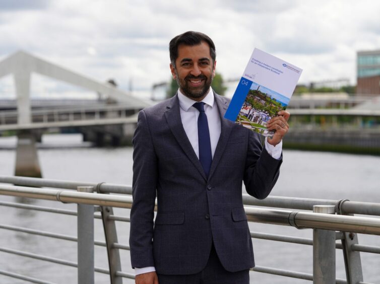 Humza Yousaf standing next to a bridge, holding the document setting out his plan for an independent Scotland to have a written constitution.