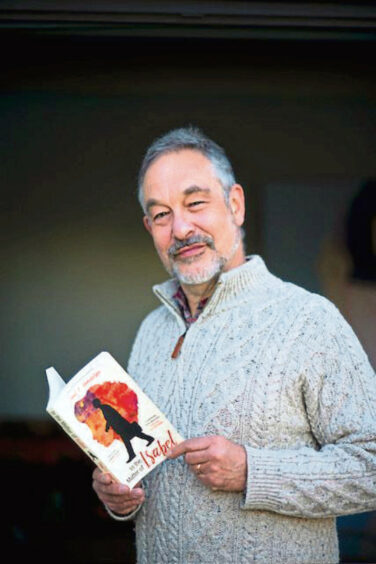 The image shows author of The Forever Moment Paul A Mendelson. Paul is holding a copy of his earlier novel In The Matter of Isabel.