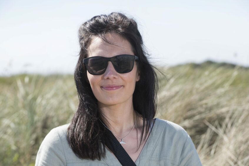 Lindsey, a woman with dark hair, stands near the coast at Carnoustie wearing black sunglasses. She has been working to protect the Small Blue butterflies in Angus for six years. 
