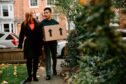 a couple walking while carrying a box to bring into their new home