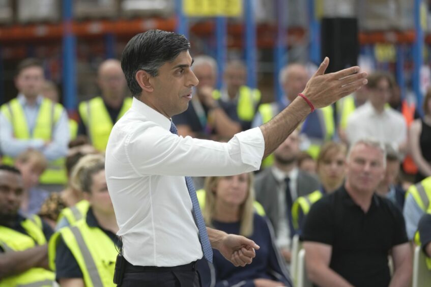 Prime Minister Rishi Sunak in white shirt and blue tie speaking to an audience of employees, most in yellow hi-vis jackets at an IKEA distribution centre in Dartford, Kent.