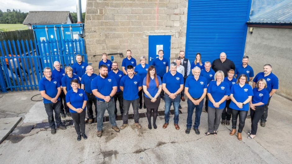 Staff of Powerwasher Services near Aberdeen stands in front of premises in blue polos, smiling up at the camera.