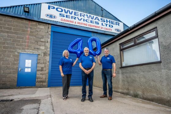 Powerwasher Services staff stands in front of sign and holds up balloons, celebrating 40 years in the business.