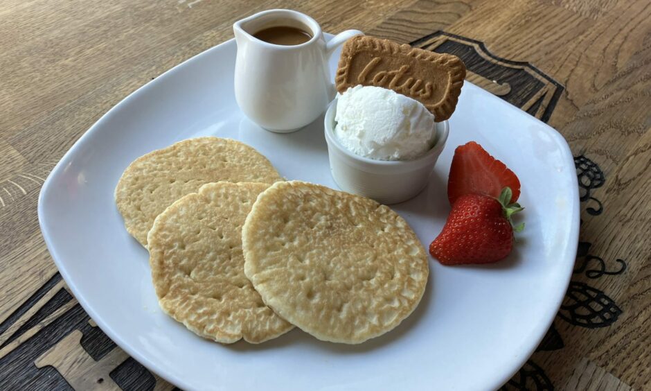 Three small pancakes, a scoop of vanilla ice cream topped with a Lotus biscuit, a strawberry and a jug of Biscoff sauce at The Tinsmith.