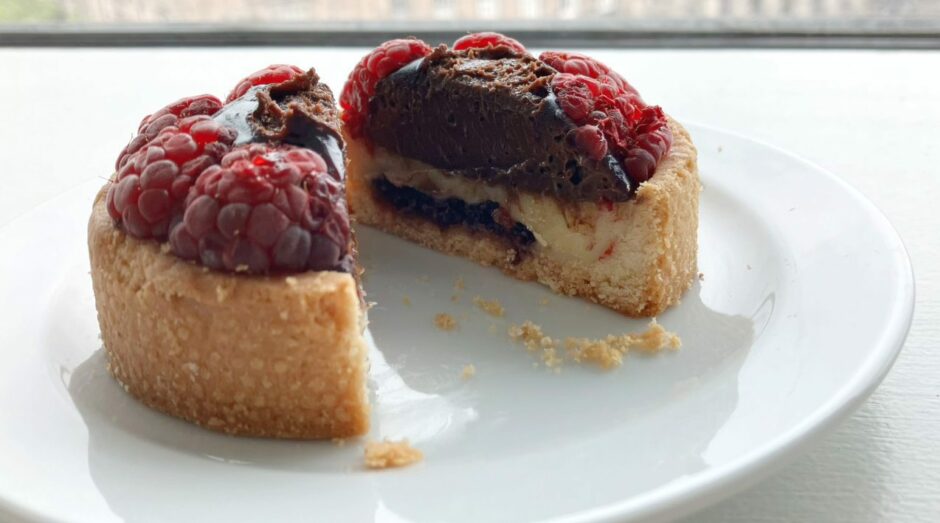 A small tart sliced in two with chocolate and raspberry filling.