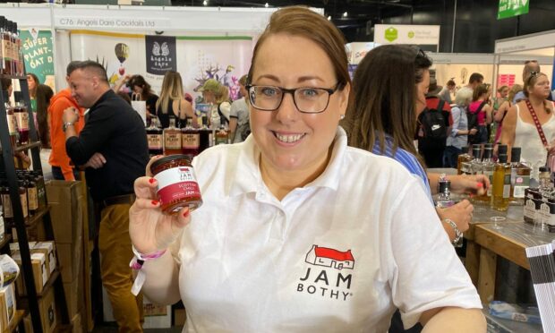A woman wearing a Jam Bothy tshirt holding up a jar of jam.
