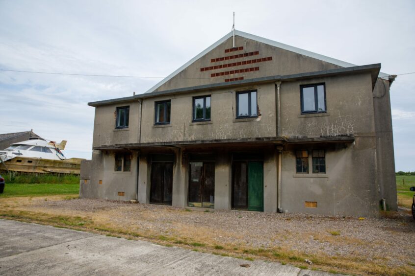 Picture shows an abandoned Second World War building called a cinasium. It look old and dilapidated and sits in countryside with grey skies in the background. 