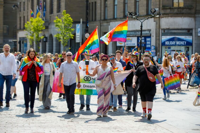 Large group of people with rainbow flags and banners walking through Dundee city centre during this year's Pride. 