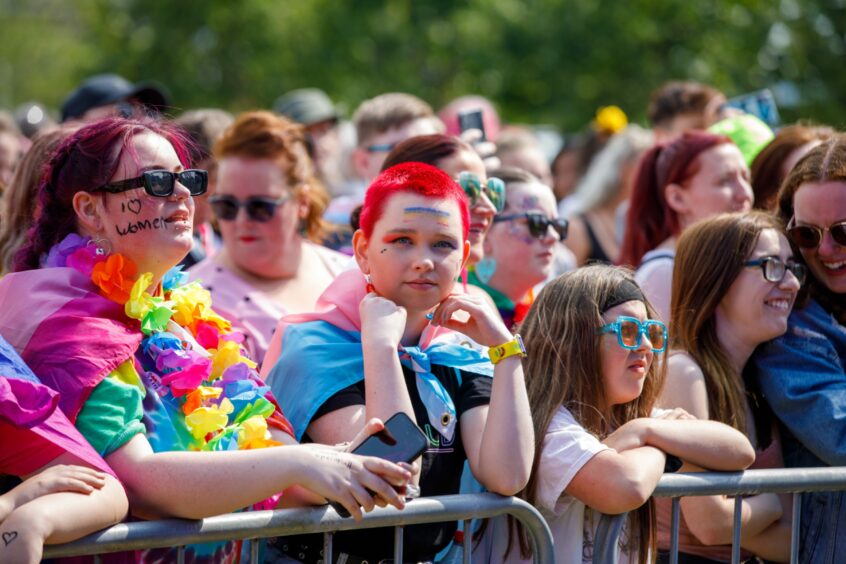 Faces in the crowds at the Dundee Pride celebrations in Slessor Gardens. A young person with close cropped orange hair and a trans flag draped around their shoulders gazes straight at the camera.