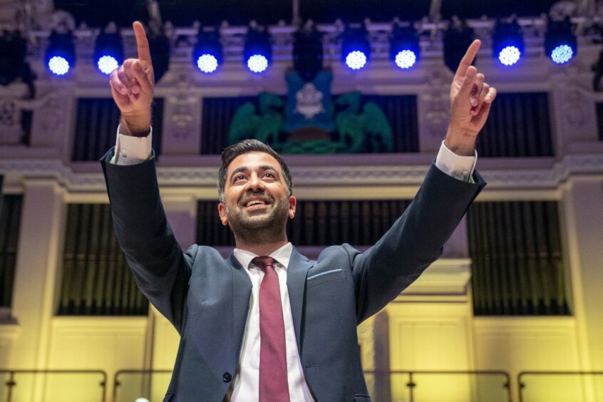 First Minister Humza Yousaf on stage after his speech at the SNP independence convention at Caird Hall in Dundee. He is smiling and holding up both hands with fingers pointed at the audience.