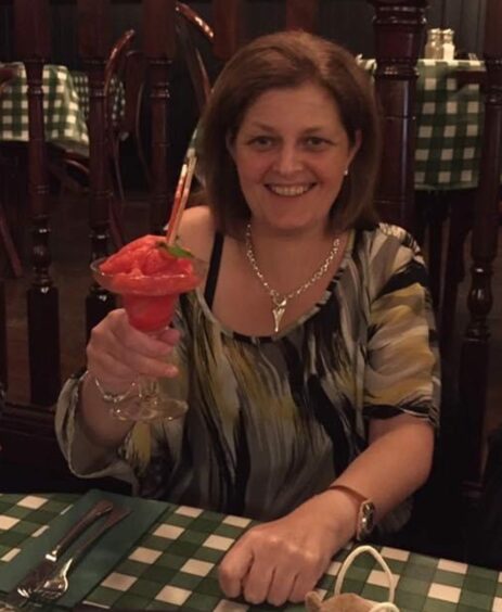 Nicola Lunn holding an ice cream sundae and smiling in a restaurant.
