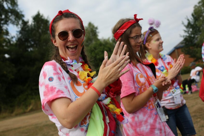 Volunteer at Over the Wall camp wearing tie-dye and a flower lei, smiling and clapping at the camera.