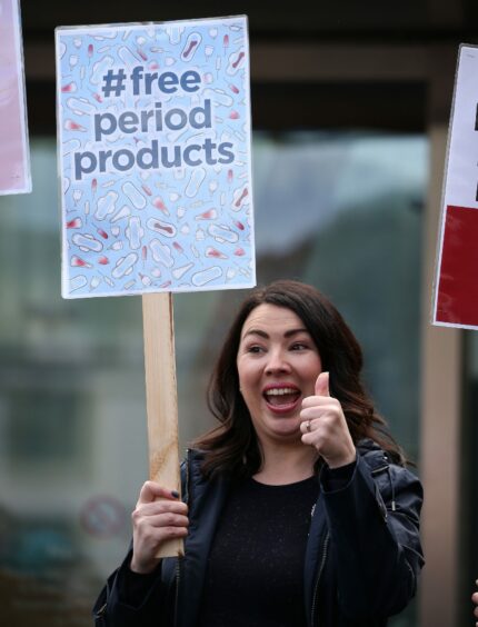 Monica Lennon MSP holding a placard which reads 'free period products'.