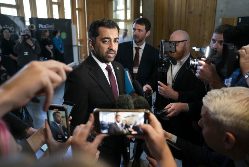 Humza Yousaf at the centre of a large group of photographers and reporters filming him on their mobile phones inside the Scottish Parliament.